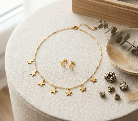 Collier étoiles et boucles d'oreilles assorties en acier doré présentés sur un guéridon avec décor minéral.