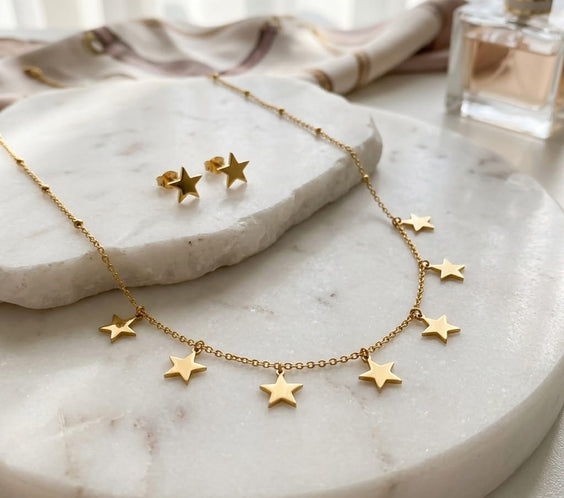 Gros plan du collier et des puces d'oreilles étoiles dorées sur un plateau en marbre.
