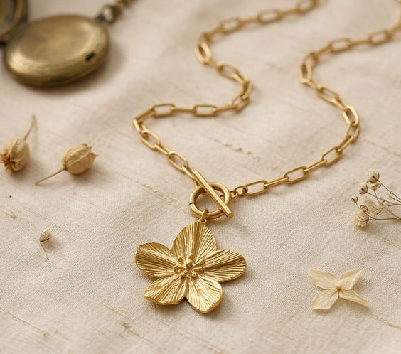 Collier pendentif fleur en or 18K porté avec un blazer beige chic.