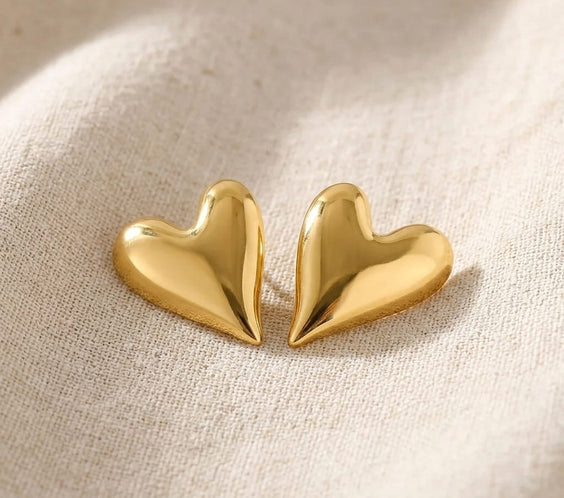 Puces d'oreilles cœur doré brillant en acier inoxydable avec leurs fermoirs papillon sur un tissu en lin beige et brin de lavande.