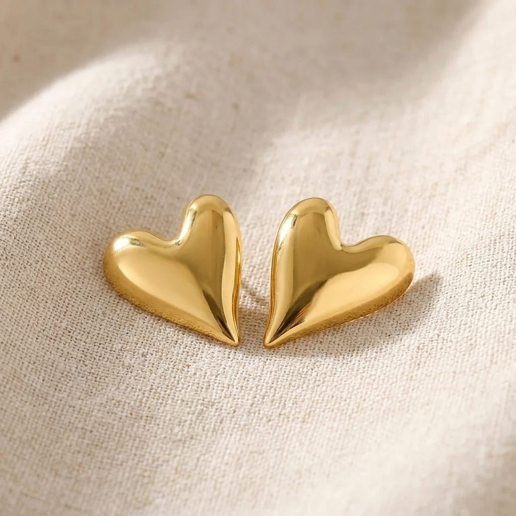 Puces d'oreilles cœur doré brillant en acier inoxydable avec leurs fermoirs papillon sur un tissu en lin beige et brin de lavande.