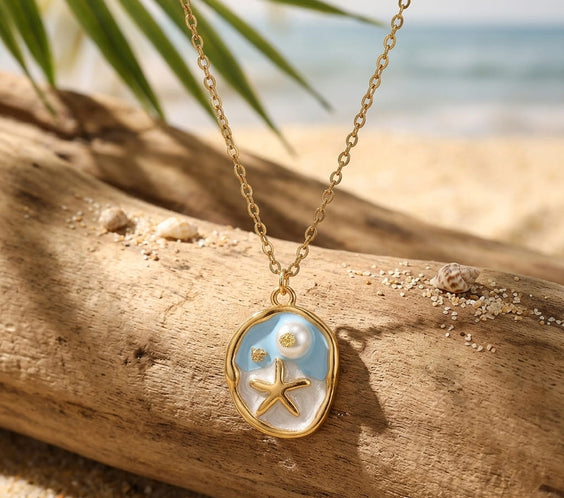 Collier médaillon ovale doré avec étoile de mer sur fond émaillé bleu et perle nacrée.