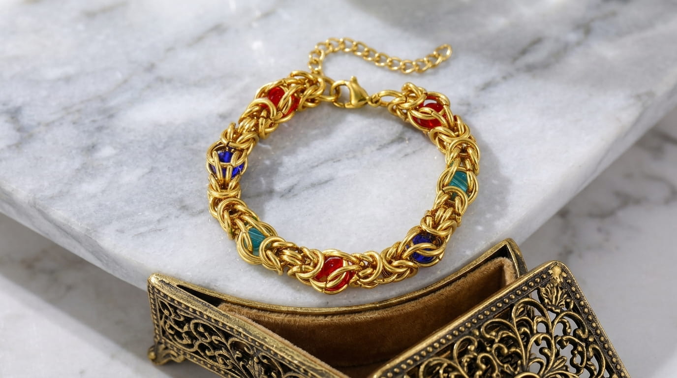 Bracelet maille byzantine doré en acier inoxydable posé sur un plateau en bois avec une fleur blanche.