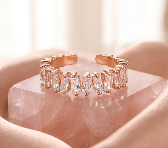 Bague ouverte en or rose avec zircons taille baguette posée sur un bloc de quartz rose.