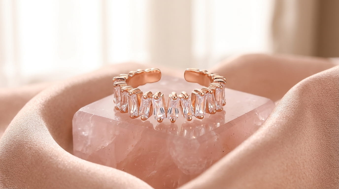 Bague ouverte en or rose avec zircons taille baguette posée sur un bloc de quartz rose.