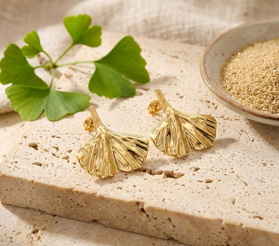 Bracelet gourmette large doré présenté sur un plateau en bois avec une fleur blanche et des livres anciens.