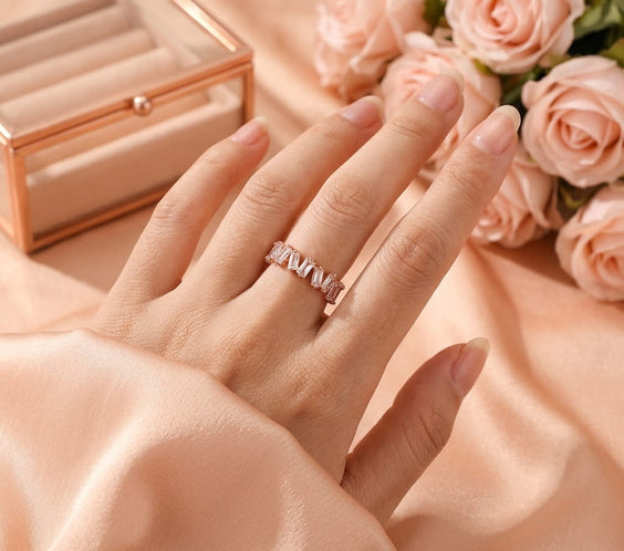 Bague or rose scintillante portée à l'annulaire dans une ambiance douce avec des roses.