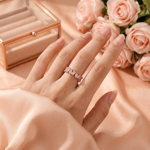 Bague or rose scintillante portée à l'annulaire dans une ambiance douce avec des roses.