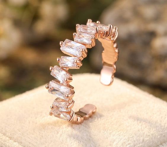 Gros plan d'une bague ajustable en or rose sertie de cristaux de zircon clairs sur un support en velours beige.