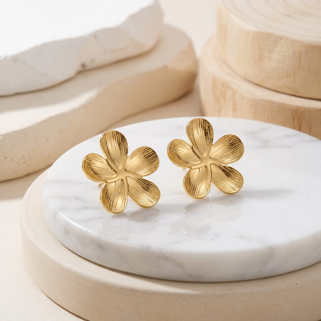 Puces d'oreilles fleur dorées en acier inoxydable posées verticalement sur un socle rond en marbre avec éléments en bois.